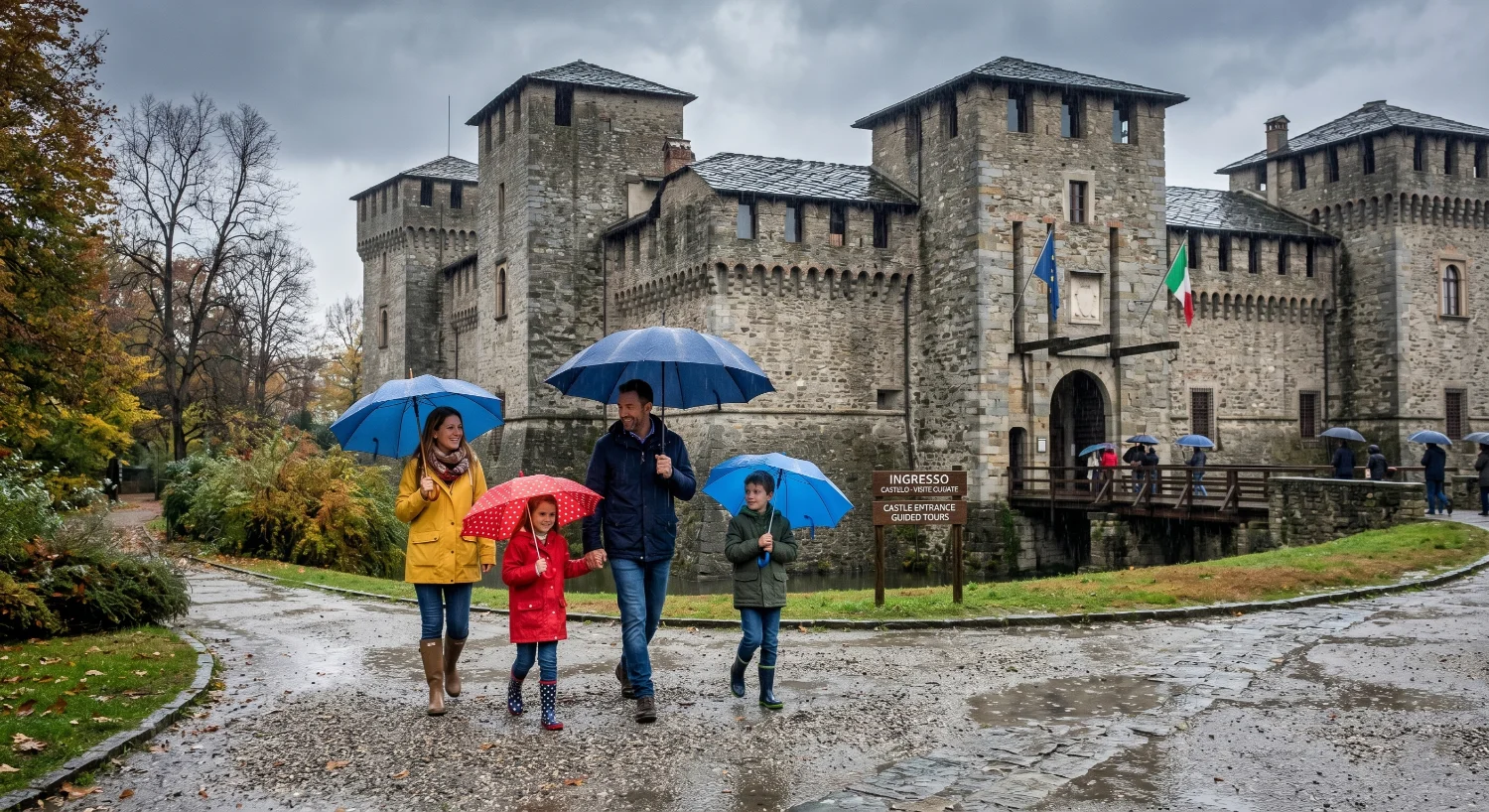 Una famiglia con bambini cammina con ombrelli colorati davanti all'ingresso di un castello medievale in una giornata di pioggia.