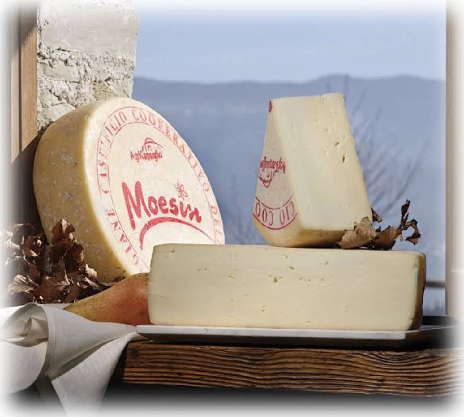 Forma intera e fette di formaggio Moesin di Fregona su vassoio di legno con una pera